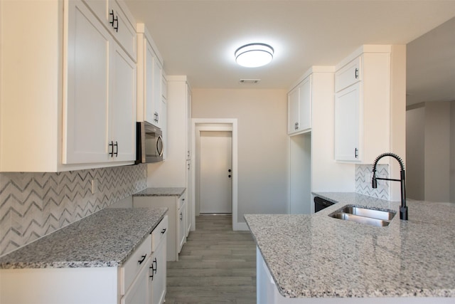 kitchen with light wood-type flooring, light stone counters, white cabinetry, and sink