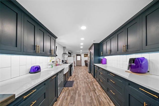 kitchen with light stone counters, wall chimney exhaust hood, backsplash, stainless steel appliances, and hardwood / wood-style floors