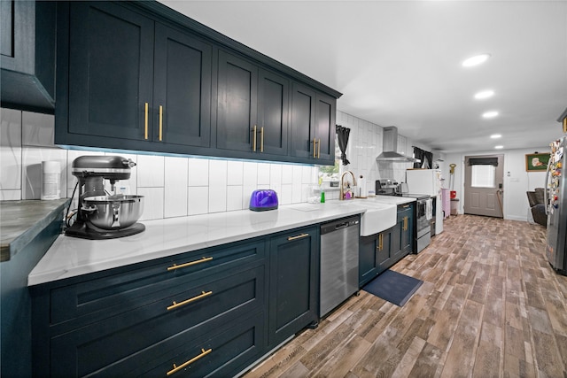 kitchen featuring appliances with stainless steel finishes, decorative backsplash, wall chimney exhaust hood, light hardwood / wood-style flooring, and sink