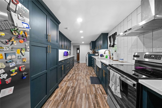 kitchen with appliances with stainless steel finishes, decorative backsplash, wall chimney exhaust hood, dark hardwood / wood-style flooring, and washer and clothes dryer