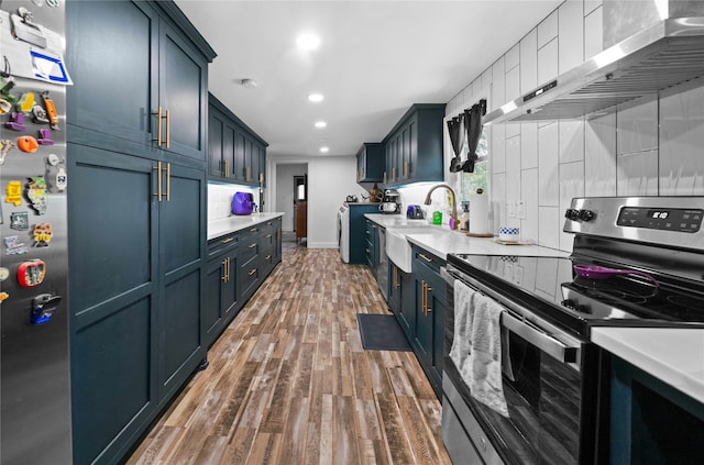 kitchen with dark wood-type flooring, sink, wall chimney exhaust hood, appliances with stainless steel finishes, and blue cabinetry