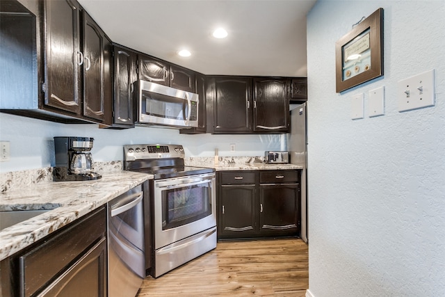 kitchen with light wood-type flooring, dark brown cabinetry, stainless steel appliances, and light stone counters