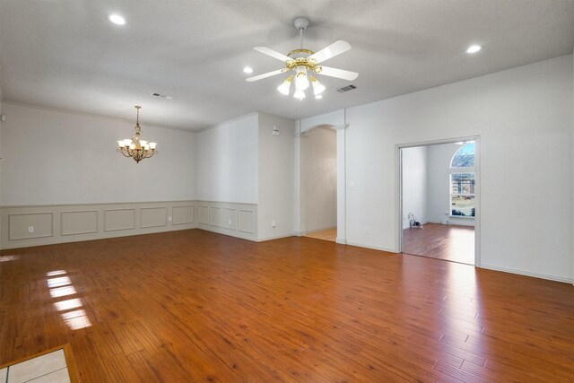 unfurnished dining area featuring a tiled fireplace, ceiling fan with notable chandelier, and light hardwood / wood-style floors