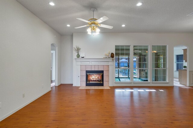 living room with a tiled fireplace, ceiling fan with notable chandelier, and light hardwood / wood-style floors