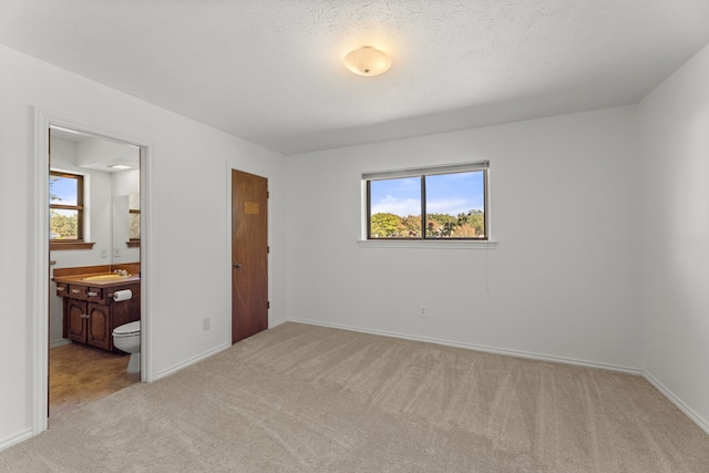 carpeted bedroom featuring a textured ceiling and ensuite bath