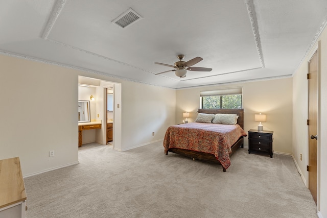 bedroom with ceiling fan, light colored carpet, a tray ceiling, and ensuite bathroom