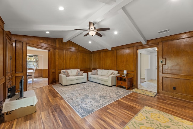 living room featuring light wood-type flooring, vaulted ceiling with beams, wood walls, and ceiling fan