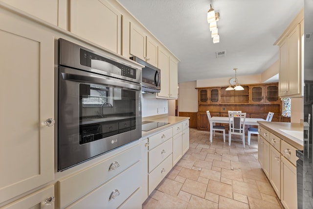 kitchen with cream cabinets, wooden walls, hanging light fixtures, and black appliances