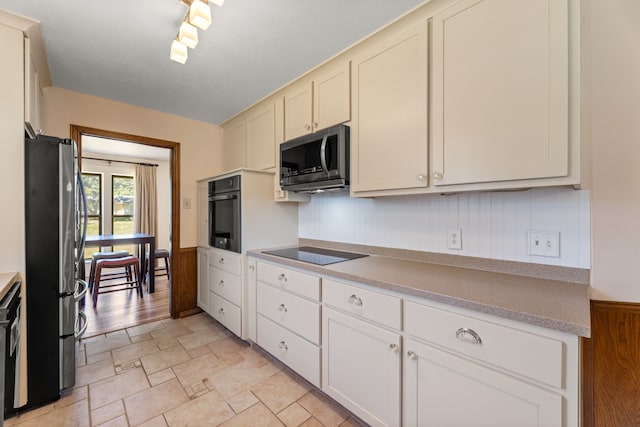 kitchen featuring rail lighting, wooden walls, and black appliances