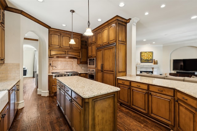 kitchen featuring hanging light fixtures, stainless steel appliances, a center island, light stone countertops, and dark hardwood / wood-style flooring