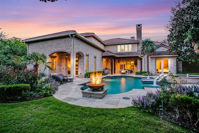 back house at dusk featuring a swimming pool with hot tub, a patio, and a lawn