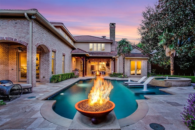 pool at dusk with an in ground hot tub, a patio area, and pool water feature