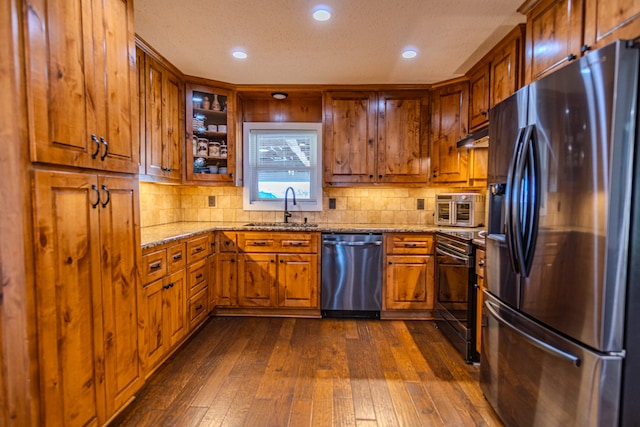 kitchen with tasteful backsplash, dark wood-type flooring, sink, stainless steel appliances, and light stone countertops