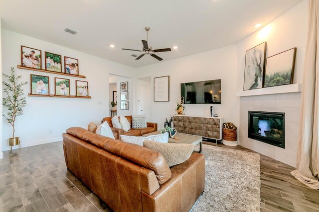 living room with light wood-type flooring, ceiling fan, and a tiled fireplace