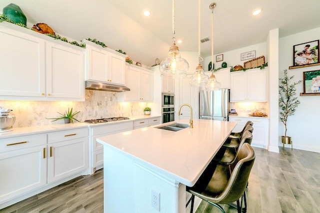 kitchen with stainless steel appliances, white cabinetry, sink, and a center island with sink