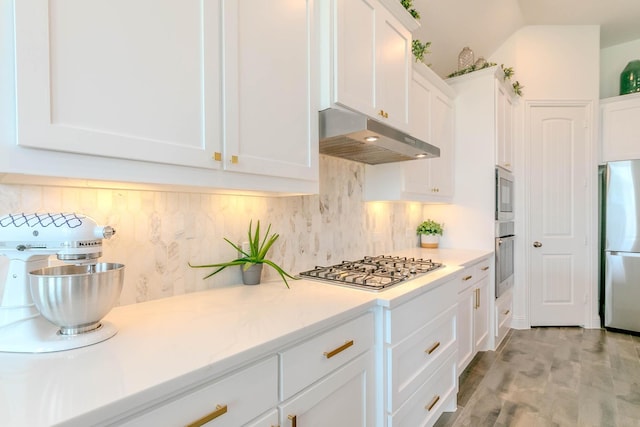 kitchen with vaulted ceiling, tasteful backsplash, white cabinetry, light hardwood / wood-style flooring, and stainless steel appliances