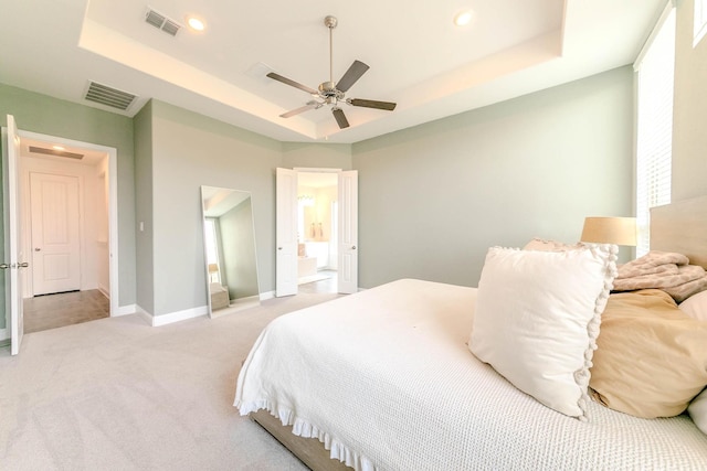 carpeted bedroom with ceiling fan, ensuite bath, and a tray ceiling