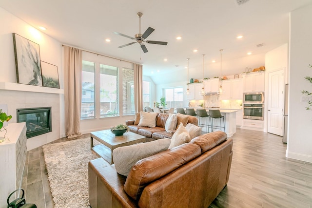 living room featuring a tiled fireplace, ceiling fan, and light hardwood / wood-style floors