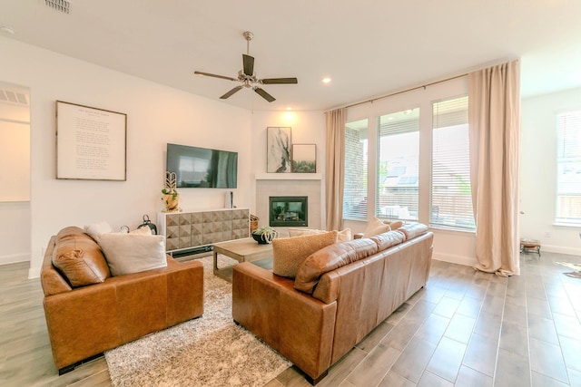 living room featuring a tiled fireplace, ceiling fan, and light hardwood / wood-style floors