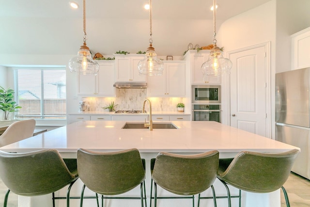 kitchen featuring fridge, stainless steel oven, a kitchen island with sink, and white cabinets