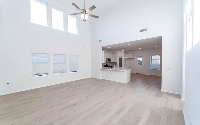 unfurnished living room featuring a towering ceiling, light hardwood / wood-style flooring, and ceiling fan