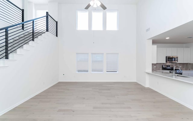 unfurnished living room with ceiling fan, sink, a high ceiling, and light hardwood / wood-style flooring