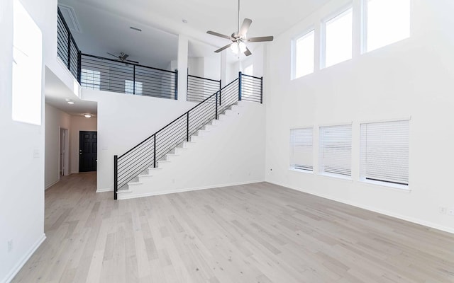 unfurnished living room with ceiling fan, light wood-type flooring, and a high ceiling