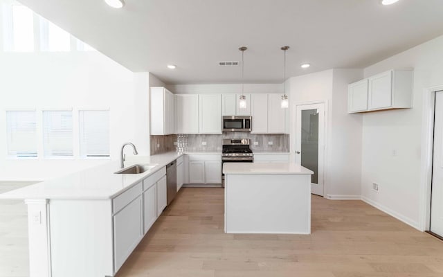 kitchen with white cabinetry, sink, hanging light fixtures, a kitchen island, and appliances with stainless steel finishes