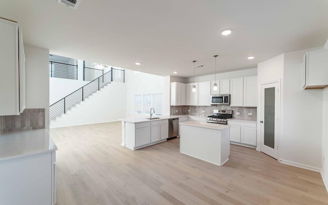 kitchen with pendant lighting, white cabinets, sink, a kitchen island, and stainless steel appliances