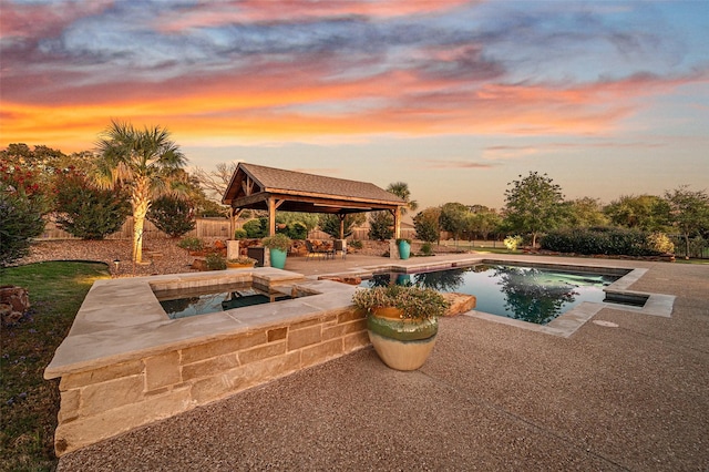 pool at dusk featuring a gazebo, an in ground hot tub, and a patio