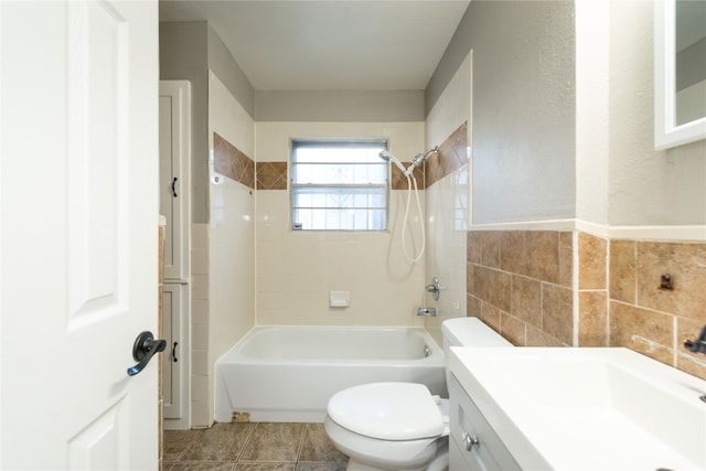 full bathroom with tile walls, tile patterned flooring, tiled shower / bath combo, vanity, and toilet