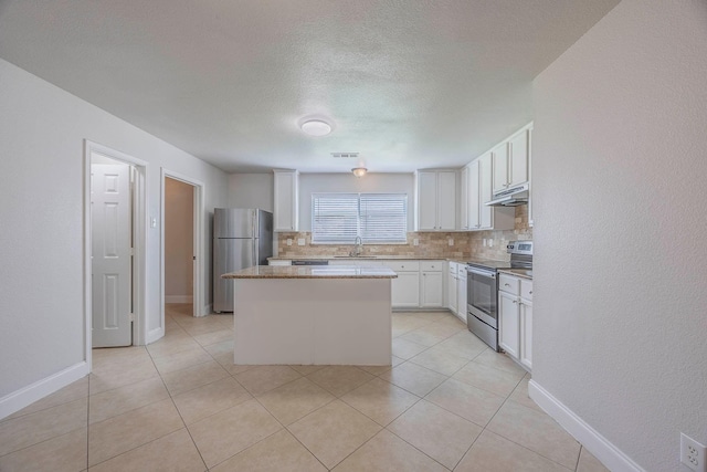 kitchen with stainless steel appliances, under cabinet range hood, a kitchen island, backsplash, and a sink