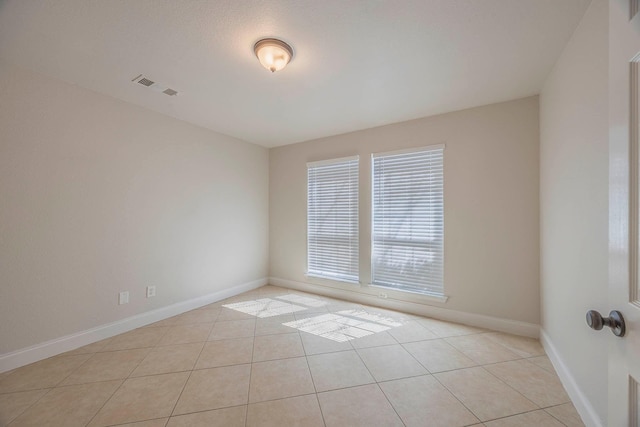 empty room featuring baseboards, visible vents, and light tile patterned flooring