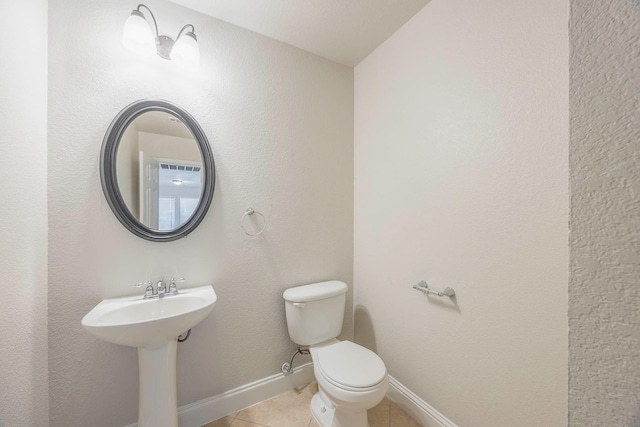 half bathroom featuring tile patterned floors, baseboards, toilet, and a sink