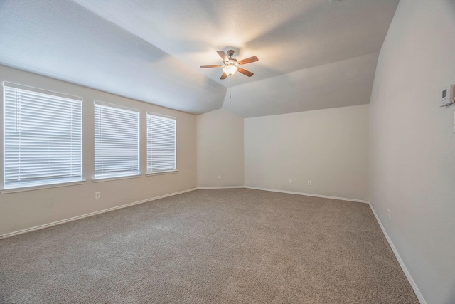 empty room featuring lofted ceiling, carpet, ceiling fan, and baseboards