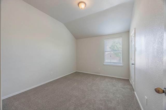 carpeted empty room featuring lofted ceiling and baseboards