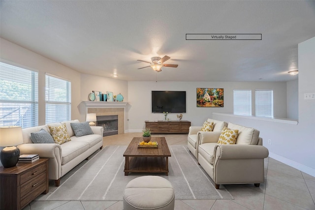living area with light tile patterned floors, a fireplace, a ceiling fan, and baseboards