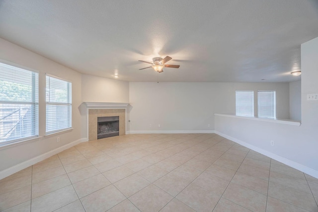 unfurnished living room with a tiled fireplace, baseboards, ceiling fan, and light tile patterned flooring