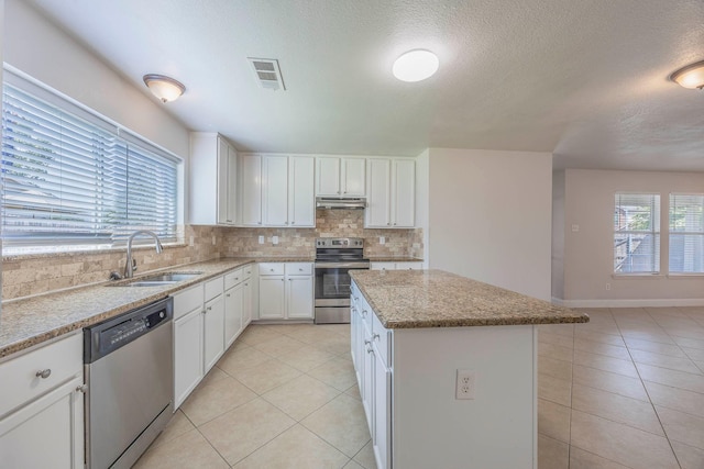 kitchen featuring light tile patterned floors, stainless steel appliances, under cabinet range hood, and a sink