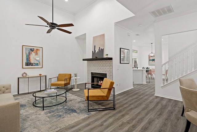 living room with ornamental molding, a high ceiling, a tile fireplace, and hardwood / wood-style floors