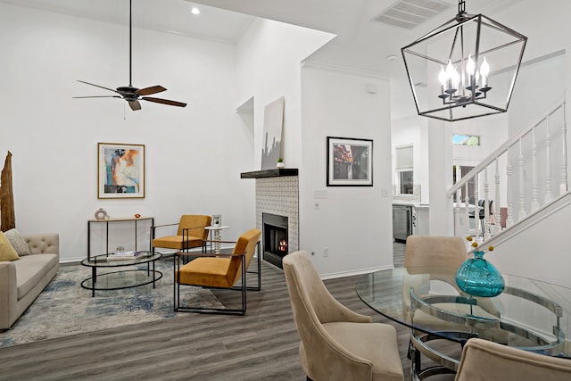 living room with crown molding, dark wood-type flooring, ceiling fan with notable chandelier, and a fireplace