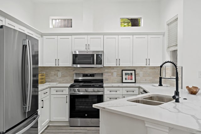 kitchen featuring sink, appliances with stainless steel finishes, light stone countertops, decorative backsplash, and white cabinets