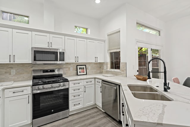 kitchen with appliances with stainless steel finishes, white cabinetry, sink, kitchen peninsula, and light stone countertops