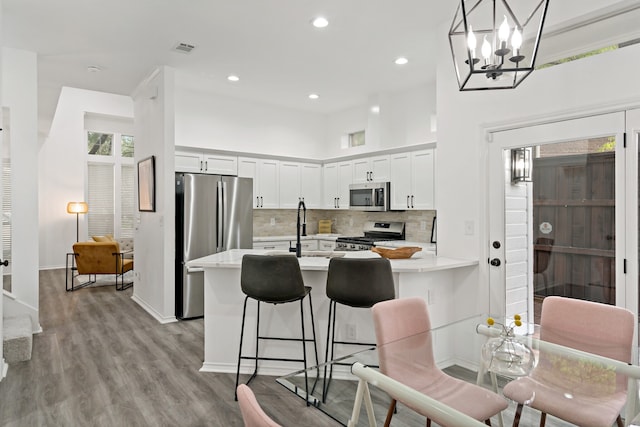 kitchen with white cabinetry, stainless steel appliances, a kitchen bar, decorative light fixtures, and light wood-type flooring