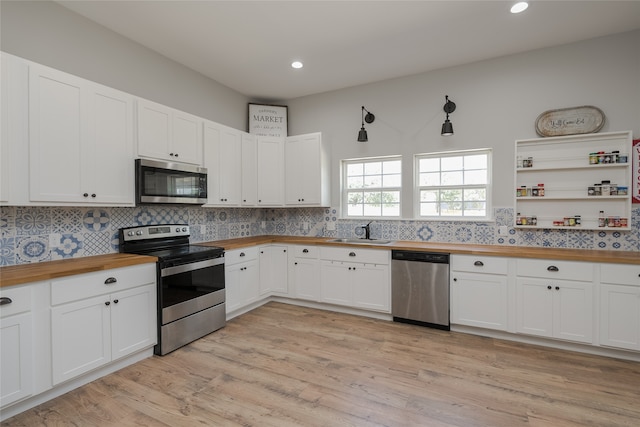 kitchen with appliances with stainless steel finishes, white cabinets, light wood-type flooring, wood counters, and sink