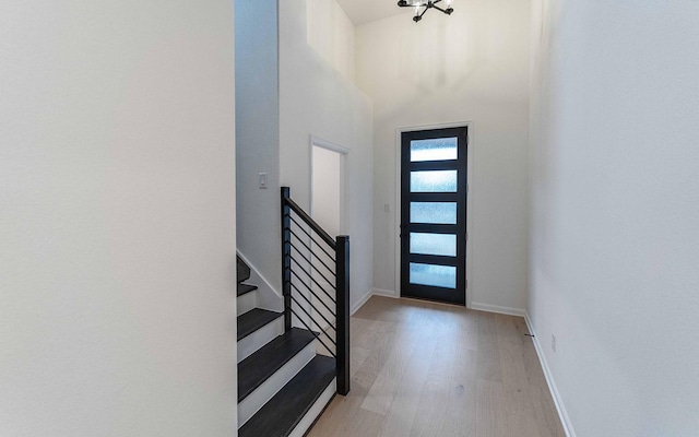 foyer featuring light wood-style floors, baseboards, a high ceiling, and stairway