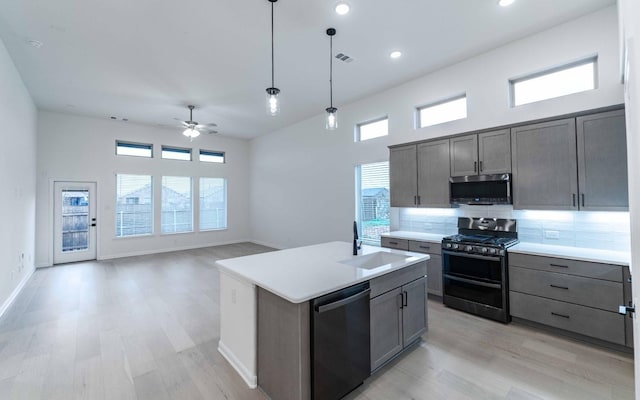 kitchen with light countertops, appliances with stainless steel finishes, open floor plan, a sink, and an island with sink