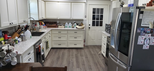 kitchen with light stone counters, wood-type flooring, backsplash, white cabinetry, and stainless steel appliances