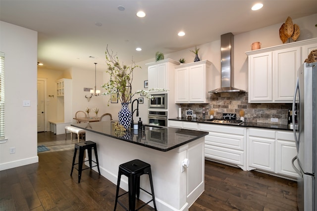 kitchen with a kitchen island with sink, wall chimney range hood, stainless steel appliances, and white cabinets