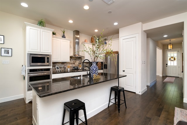 kitchen featuring appliances with stainless steel finishes, white cabinetry, dark hardwood / wood-style flooring, and wall chimney range hood